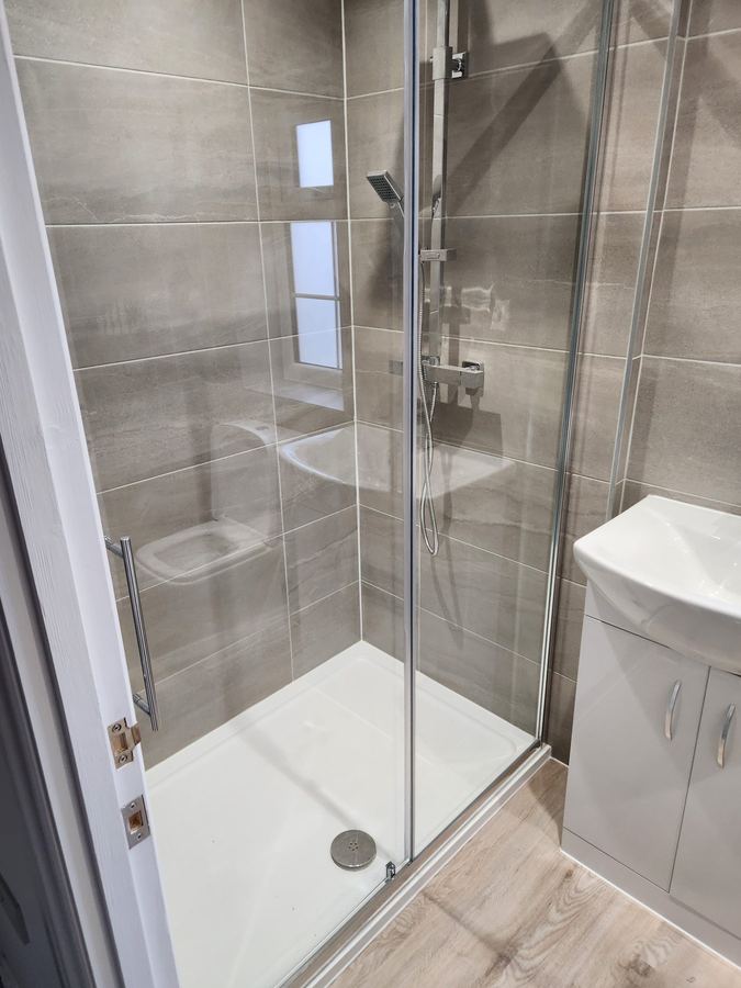 Shower room with a sliding glass enclosure and stone effect tiling